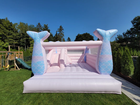 Inflatable bounce house with mermaid tail design on a grassy area with trees in the background